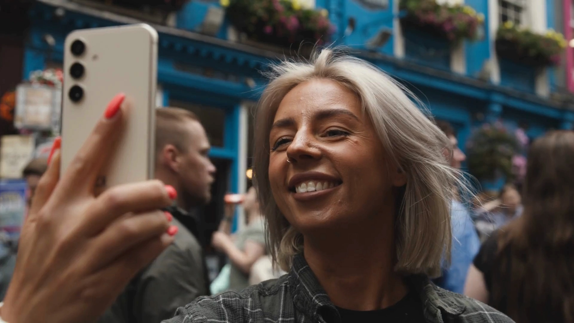 Young woman video-calling on her smartphone in Edinburgh city centre with people walking behind her.