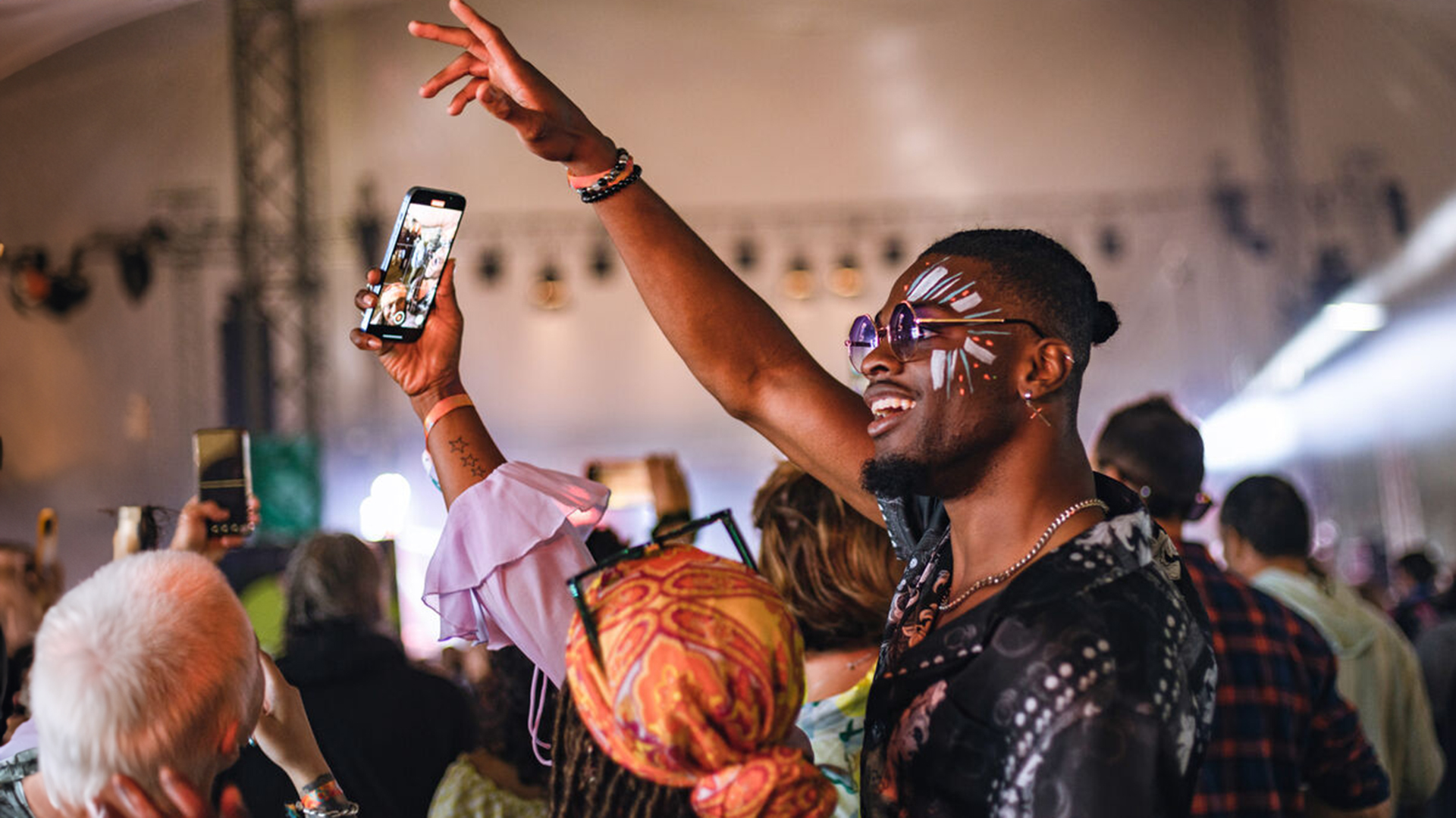 Young couple smiling while taking a selfie on a smartphone at a music festival.