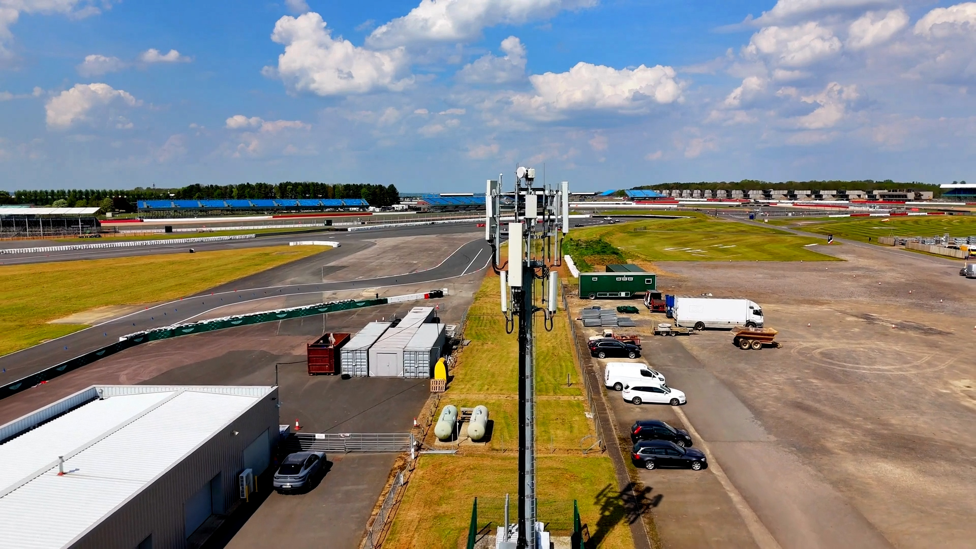 EE mobile mast at Silverstone racetrack with cars racing in the background.