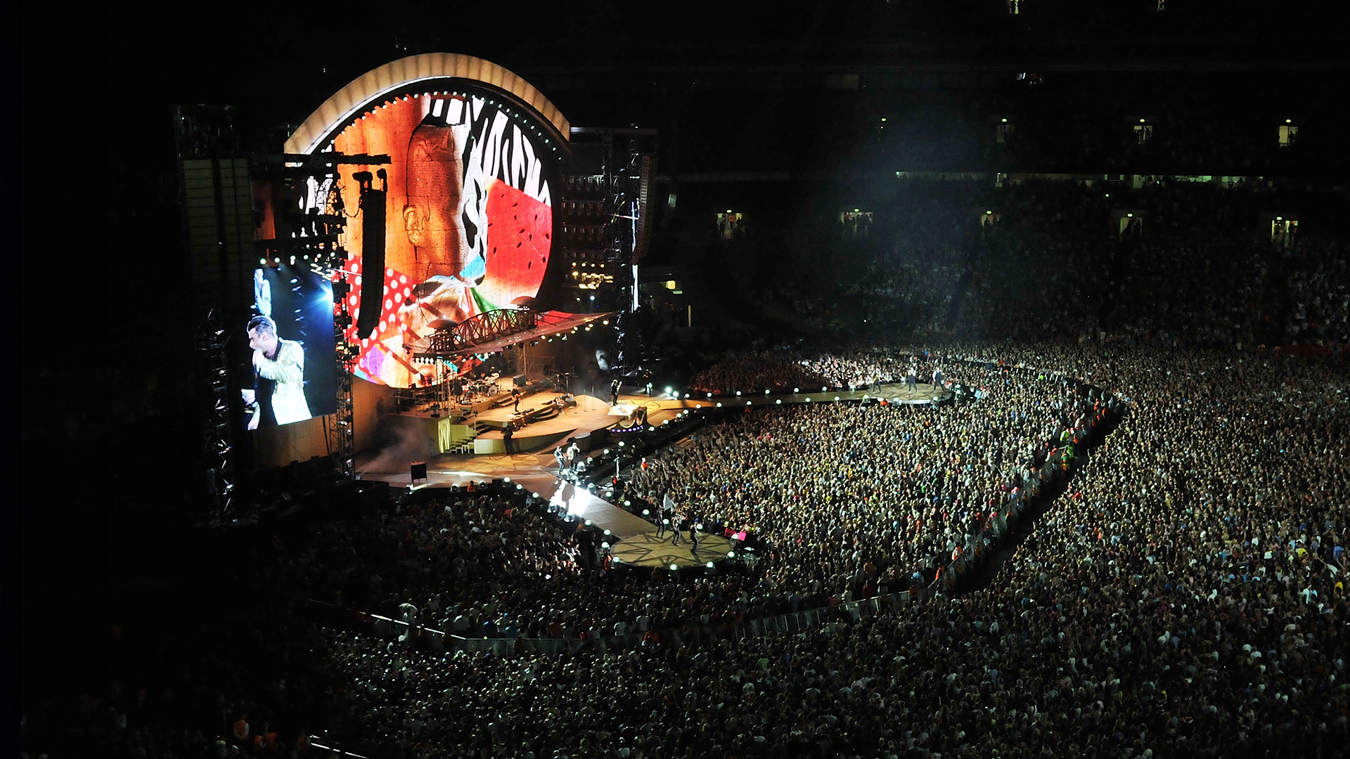 Robbie Williams performing on stage in front of a sold-out arena.