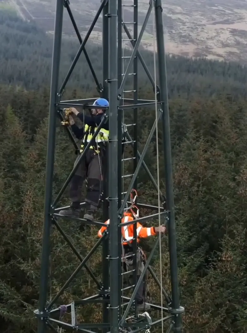 An Openreach engineer works on connections inside a street cable box, consulting diagnostic equipment.