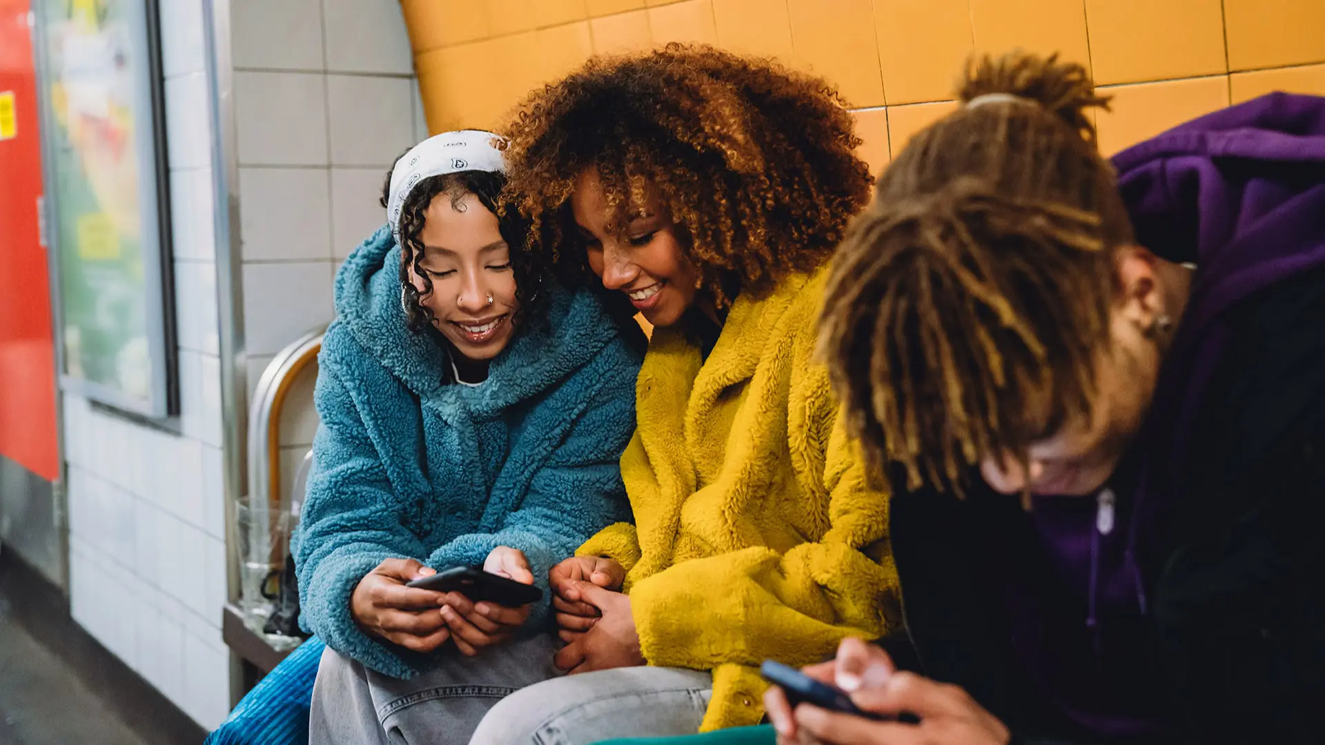 A teenager shows content on her mobile phone to her friends, while waiting for a train on a London underground tube platform. 