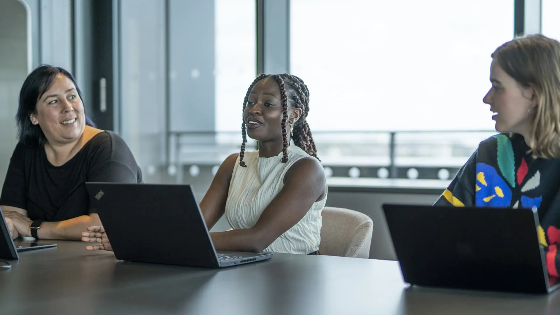 A young woman speaks confidently at a meeting in an office. Her female colleagues listen intently.