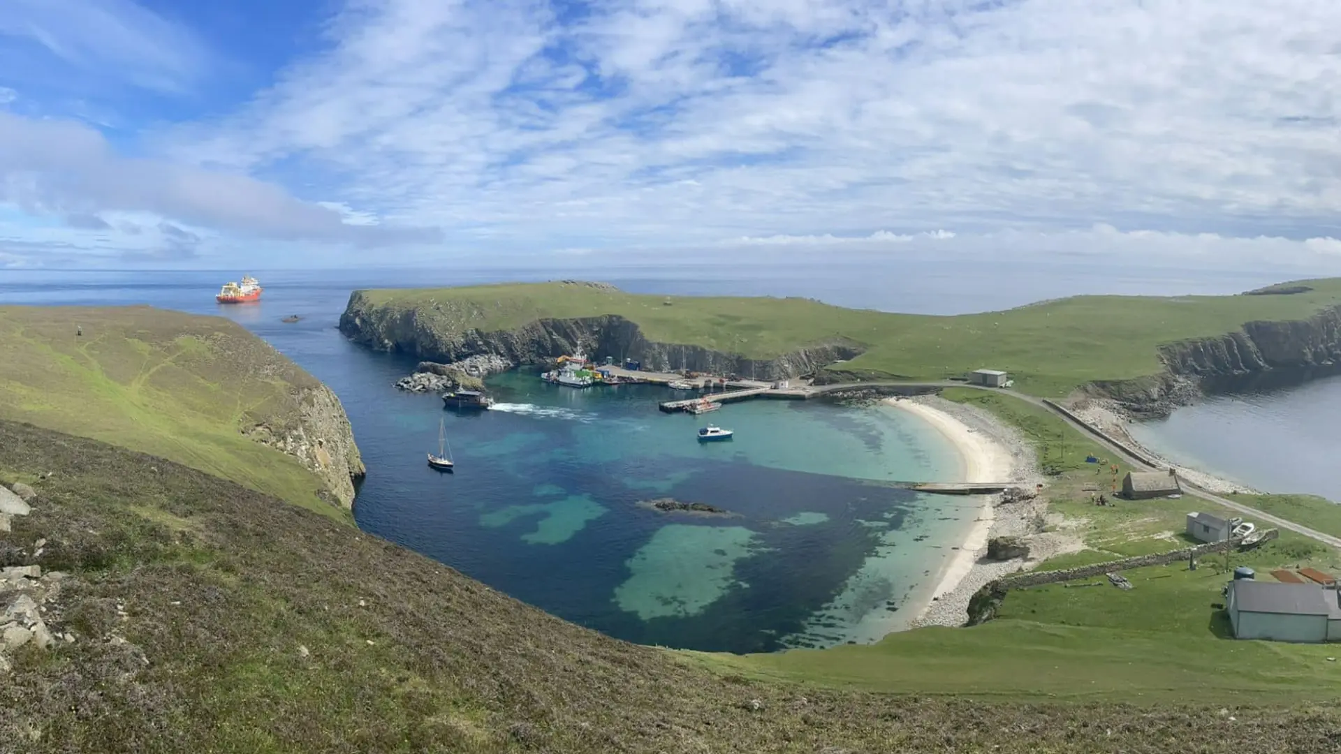 A lighthouse and a stone house stand in a grassy Fair Isle landscape